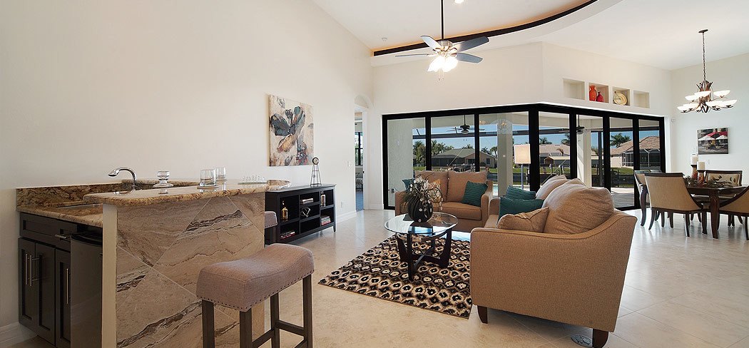 Open living room with a stone wet bar and sliding glass walls to the pool