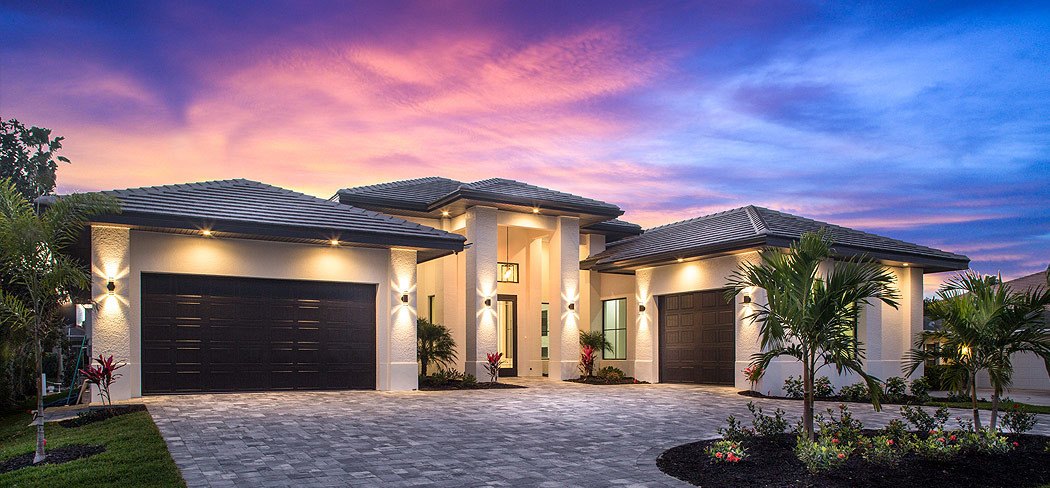 Single-story home at dusk with twin garages, a paver driveway and lit palms