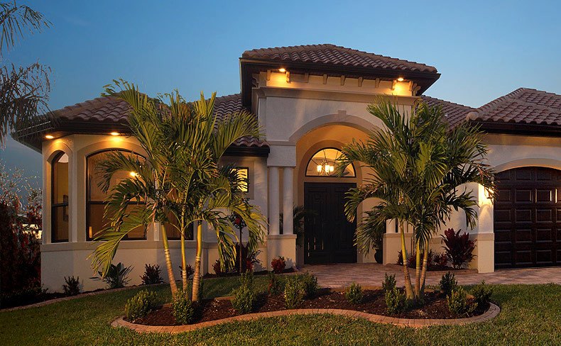 Tile-roof home at dusk with an arched entry, lit sconces and palms