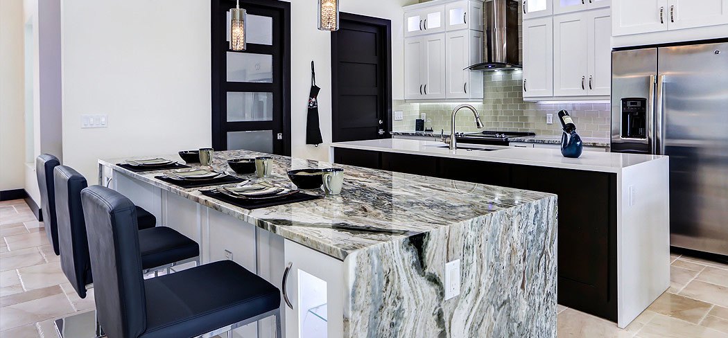 Kitchen with a waterfall stone island, white upper cabinets and stainless appliances